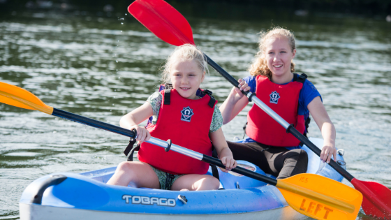 Two young girls are wearing life jacket and smiling as they kayak