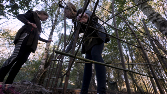 Two teenage girl build a structure with branches